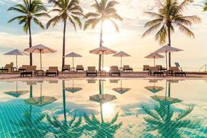 beau parasol et chaise de luxe autour de la piscine extérieure de l'hôtel et du complexe avec cocotier au coucher du soleil ou au lever du soleil