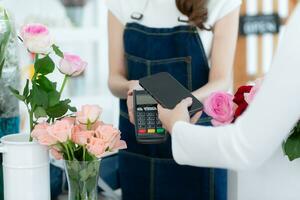 tondu coup de femelle fleuriste en portant téléphone intelligent payant pour fleurs dans fleur magasin photo