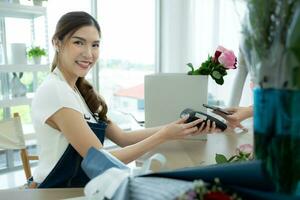 tondu coup de femelle fleuriste en portant téléphone intelligent payant pour fleurs dans fleur magasin photo