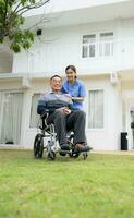 souriant infirmière et Sénior homme séance dans une fauteuil roulant dans le jardin photo