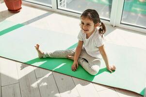 mignonne peu fille repos sur exercice tapis à Accueil sur une magnifique ensoleillé journée photo