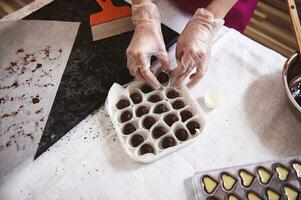 Haut vue de chocolatier mains dans blanc transparent gants emballage Chocolat truffes dans boîte mensonge suivant à moules avec salé caramel remplissage photo