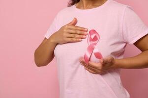 femme met mains en dessous de rose ruban sur sa rose t chemise, justificatif Sein cancer conscience campagne. concept de 1 st octobre rose mois, aux femmes santé se soucier, colorecd arrière-plan, copie espace. fermer photo