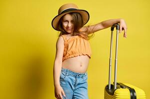 content enfant fille avec élégant valise, joliment sourit à caméra plus de Jaune Contexte. voyage, des gamins et été concept photo