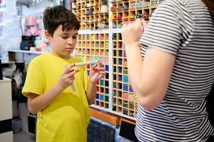 sérieux adolescent garçon choisit aquarelle Marqueurs dans école papeterie magasin, demande une Ventes directeur pour Aidez-moi photo