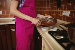 côté vue de confiseur dans rose tablier mélange fondu Chocolat Masse dans bol avec une en bois spatule photo