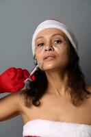 jolie femme dans Père Noël costume et lissage patchs en dessous de yeux, détient seringue avec beauté injection. peau se soucier rajeunissement, anti-âge se soucier. studio coup pour beauté spa salons pour Noël cadeaux photo