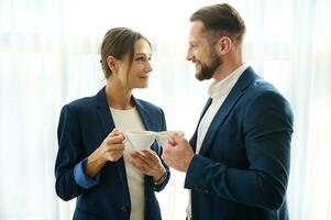 concept de l'amour affaires et intimité à travail. attrayant Jeune femme flirte avec sa collègue, affaires partenaire plus de une tasse de café dans une Hôtel pièce tandis que permanent suivant à chaque autre par le fenêtre photo