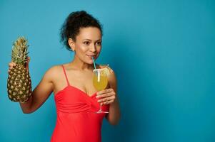 Jeune femme avec une ananas en buvant une délicieux exotique cocktail de une paille, posant plus de bleu Contexte photo