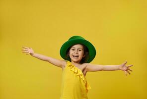 mignonne fille dans vert lutin irlandais chapeau propager sa mains large et sourit à le caméra posant sur une Jaune Contexte. Saint patrick's journée. photo