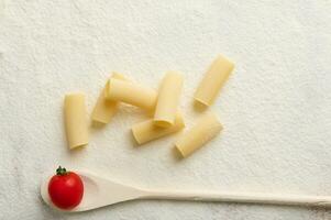 plat allonger composition avec brut italien Pâtes- tortiglioni- et une petit tomate sur une en bois cuillère sur une blanc fariné Contexte avec copie espace. nourriture Contexte photo