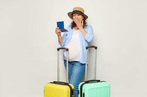 étonné Enceinte femme avec deux les valises, en voyageant à l'étranger dans grossesse temps, en portant passeport plus de blanc Contexte. photo