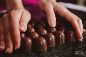 femelle mains avec fait maison Chocolat pralines sur une marbre surface pour trempe fondu Chocolat masse. fermer photo