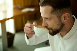 affaires voyage et gens concept. fermer portrait de attrayant charmant Beau réussi caucasien barbu homme d'affaire en buvant fraîchement brassée café à Hôtel chambre, pour parfait début de le journée photo