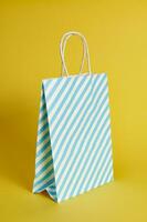 bleu blanc rayé papier cadeau sac sur une Jaune arrière-plan, coup avec une lumière ombre. copie espace pour La publicité photo