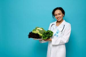 magnifique mixte course femme nutritionniste dans médical robe et bleu Diabète conscience ruban pose avec assiette de en bonne santé brut nourriture contre une bleu Contexte avec copie espace pour médical La publicité photo