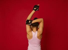 arrière vue de un actif femme dans tenue de sport et écouteurs élongation bras, exercice contre rouge Contexte avec copie un d espace photo