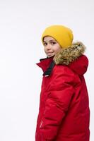 côté portrait de une Beau enfant, adorable préadolescent garçon dans brillant Jaune de laine chapeau et rouge vers le bas veste à la recherche par le sien épaule à caméra, isolé plus de blanc Contexte. copie un d espace photo