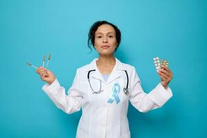 monde Diabète journée. 14 novembre. femelle médecin dans blanc médical robe portant bleu conscience ruban détient insuline seringues, pharmaceutique comprimés dans ampoules, isolé sur bleu arrière-plan, copie espace photo