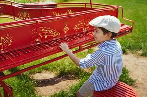 une écolier effectue une chanson sur une Stationnaire rouge piano dans le jardin photo