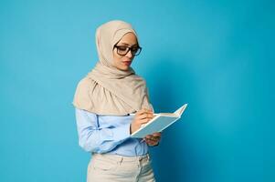 musulman femme portant lunettes et strict tenue avec couvert tête l'écriture sur une blanc livre photo