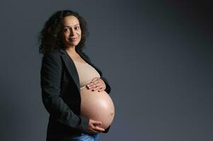 authentique souriant content Enceinte femme en portant sa nu ventre, à la recherche à caméra, isolé gris Contexte. grossesse photo