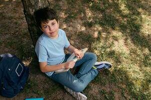 vue de au dessus de une école enfant, adorable préadolescent garçon dans décontractée jean, en train de lire livre après école dans le arrière-cour photo