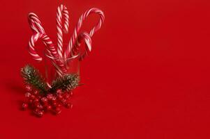 studio coup de magnifique minimaliste Facile composition avec Noël sucettes dans transparent verre et neigeux branche de pin avec rouge baies, houx, sur rouge Contexte avec copie espace pour un d photo