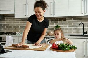 maman et fille cuisinier Pizza ensemble, rouleau en dehors le pâte avec une en bois roulant épingle et avoir amusement ensemble dans le cuisine photo