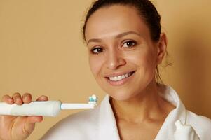 isolé portrait sur beige Contexte de un attrayant femme avec magnifique à pleines dents sourire en portant une brosse à dents avec dentifrice près sa affronter. oral se soucier concepts photo