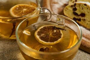 fermer de verre tasses avec à base de plantes thé avec séché Orange tranches et clous de girofle sur le Contexte de Couper fait maison traditionnel allemand pain fraîchement cuit pour Noël. nourriture et boisson Contexte photo