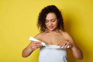 Jeune femme enveloppé dans blanc serviette pressant une dentifrice sur un électrique brosse à dents photo