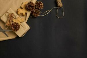 Facile minimaliste Noël composition avec Fait main pain d'épice des biscuits et présent décoré avec pin cône et lié cannelle dans une arc avec corde sur marron artisanat emballage papier avec copie un d espace photo