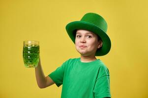 marrant garçon dans vert lutin irlandais chapeau avec une verre de vert boisson célébrer Saint patrick journée. isolé sur Jaune Contexte. photo