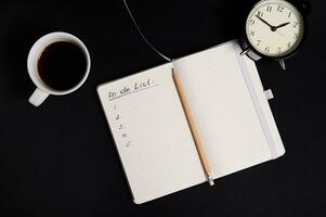 plat allonger de un ouvert organisateur, bloc-notes avec liste à faire sur Vide blanc feuilles, tasse de café et alarme l'horloge sur noir Contexte avec copie espace. entreprise, organisation, temps la gestion notions.. photo