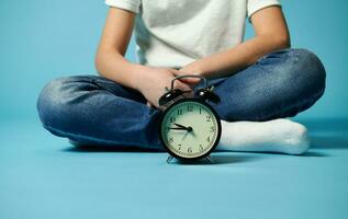 fermer de un alarme l'horloge sur le Contexte de une peu garçon séance sur bleu surface photo