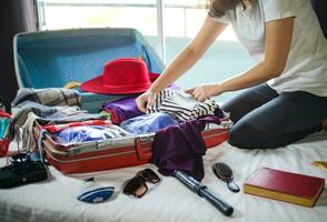 femme emballage valise sur lit pour une Nouveau périple emballage liste pour Voyage planification, en train de préparer vacances livre maintenant en voyageant transport photo