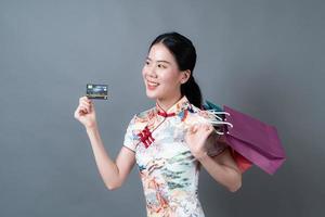 une femme asiatique porte une robe traditionnelle chinoise avec un sac à provisions et une carte de crédit photo