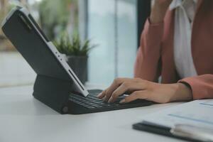 portrait d'une jeune femme asiatique pigiste à la main travaille son travail sur une tablette informatique dans un bureau moderne. faire un rapport d'analyse comptable sur les données d'investissement immobilier, le concept de systèmes financiers et fiscaux. photo