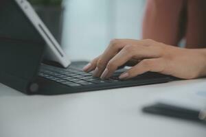 portrait d'une jeune femme asiatique pigiste à la main travaille son travail sur une tablette informatique dans un bureau moderne. faire un rapport d'analyse comptable sur les données d'investissement immobilier, le concept de systèmes financiers et fiscaux. photo