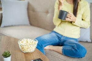 asiatique femme en train de regarder intelligent la télé et en utilisant éloigné manette main en portant télévision l'audio éloigné contrôle à Accueil avec le éloigné contrôle télévision photo