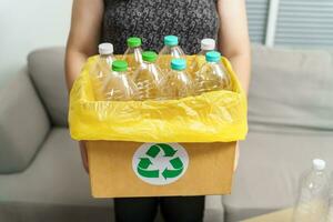 Accueil recycler éco vert zéro concept femme lancement vide Plastique bouteille dans recyclage poubelle avec Jaune des ordures Sacs à maison. photo