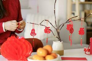 asiatique femme décoré maison pour chinois Nouveau année célébrations. en mettant traditionnel pendentif à le chinois lunaire Nouveau année pour bien chance. chinois mot veux dire bénédiction photo