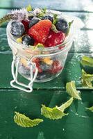 coloré mixte fruit salade dans verre récipient dans vert Contexte. photo