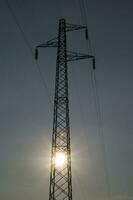 une silhouette de un électricité la tour avec le Soleil derrière il photo