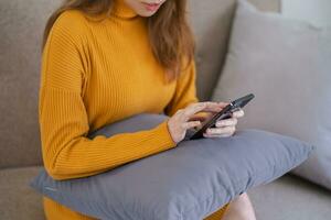 asiatique femme envoyer des SMS vérification social médias en portant téléphone intelligent à Accueil conversation avec copain ou ami. photo