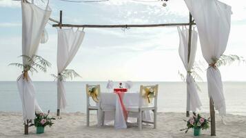 romantique dîner table ensemble et chaise préparation avec blanc thème décoration, blanc sable, clair nuageux ciel, et tranquille, pacifique, magnifique plage vue à le rivage. bien endroit pour mariage proposition photo