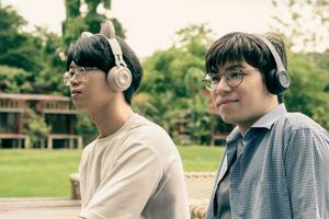 Jeune asiatique adulte couple portant écouteurs, séance, écoute à la musique et dépenses gratuit temps ensemble dans de face de leur loger, bien relation et meilleur copains concept. photo
