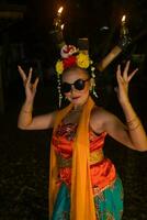un indonésien traditionnel Danseur danses dans des lunettes de soleil et un Orange costume avec une magnifique châle photo