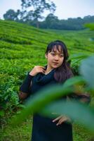 un asiatique femme dans une noir robe est posant dans de face de une très magnifique thé plantation photo